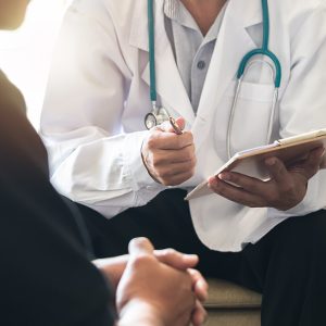 A doctor holding a clipboard and pen talks to a male patient.